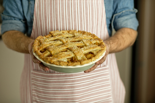 A chef in an apron holding a plate with delicious apple pie