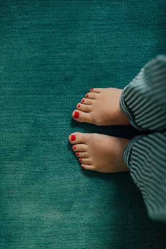 looking down at woman's feet, green striped pajamas, with coral toenails on teal rug