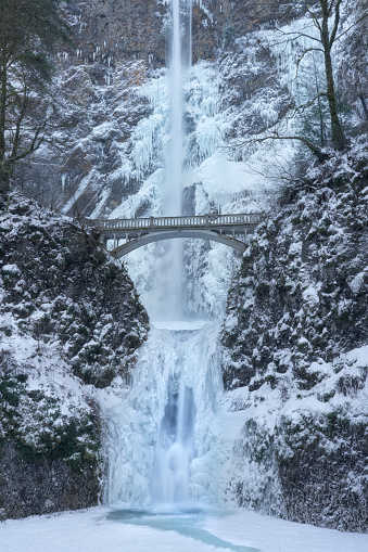 Multnomah Falls frozen during the winter of 2024. Ice and snow cover the rocks and bridge around the waterfall.