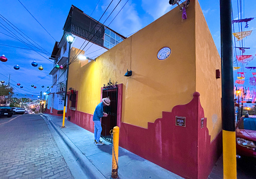 Xochimilco, Oaxaca, Mexico: A man unlocking the door of a colorful building in Xochimilco, a neighborhood known for its brightly colored walls. Sheets of papel picado, a Mexican folk art, decorate the sky on the right.