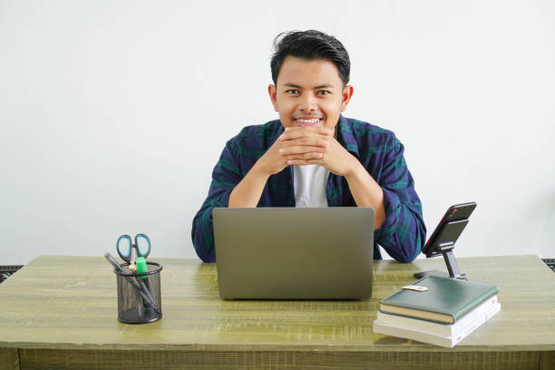 職場で笑顔のフリーランサーアジア人男性幸せな表情を見てカメラ隔離 - looking at camera smiling desk isolated ストックフォトと画像