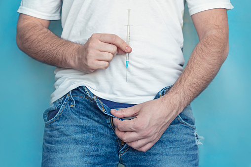 concept of protection of sexually transmitted infections. a man holds a syringe in his hands and takes off his jeans. The concept of treatment of sexually transmitted diseases.