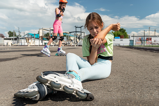 a schoolgirl girl without protective equipment fell on the asphalt while roller skating at the stadium. children ride in a skate park. dangerous entertainment.