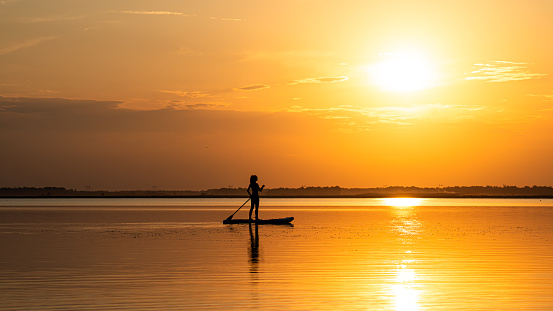 Girl paddling on SUP board on beautiful lake during sunset or sunrise, standing up paddle boarding morning adventure in lake district
