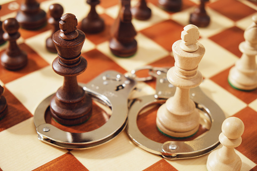 Metal handcuffs with chess pieces of kings on a chessboard, close-up.