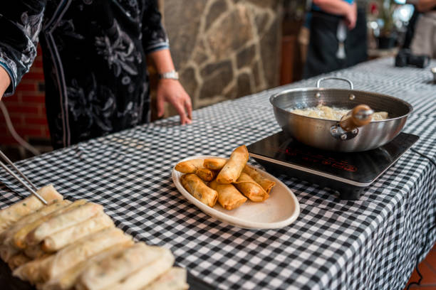 Chinese female chef is demonstrating how to pan-fry Chinese spring rolls in the kitchen on a cooking class.