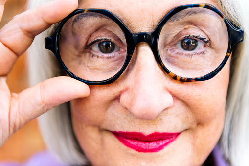 close up portrait of a beautiful senior woman putting on glasses looking at camera, concept of eye health in elderly people and active lifestyle