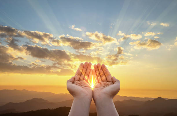 istock Human hands with bright sunbeam praying to god on mountain sunset background 2049136416