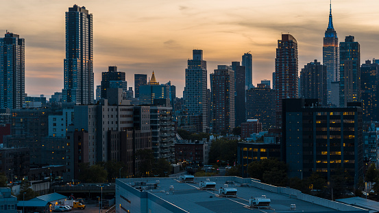Residential area of Long Island City at the front with luxury Hunters Point apartments at sunset. Midtown Manhattan with popular Empire State Building distant view.