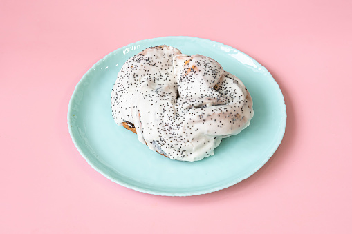 Sweet bun with poppy seeds in white cream on a pink background