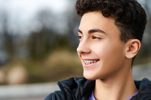 Portrait of positive happy boy, handsome teenager with braces looking away, wearing casual outfit standing on urban street. Advertisement concept, dental care