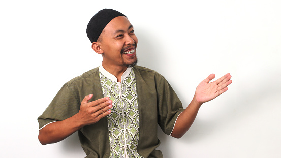 Indonesian Muslim man in koko shirt and peci extends his arms wide in a welcoming gesture, leaving space for text or advertisement. Isolated on a white background