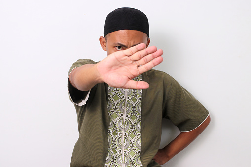 Indonesian Muslim man in koko shirt and peci crosses his arms in a stop gesture. Isolated on White background