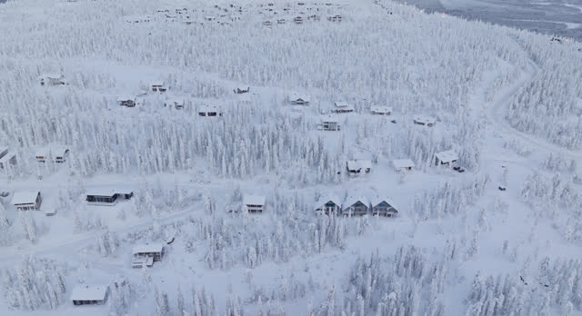 Aerial tracking shot of mountain lodges on the side of a fell, winter in Lapland