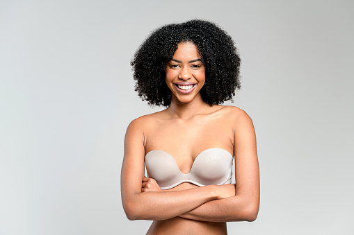 With arms crossed and a bright smile, an African-American woman stands confidently in a strapless top, embodying empowerment and self-assurance