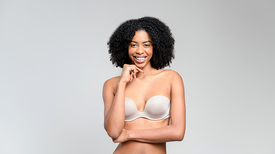 With an exuberant smile and hand near chin, this African-American woman in a strapless top radiates happiness and casual confidence, against a soft gray backdrop