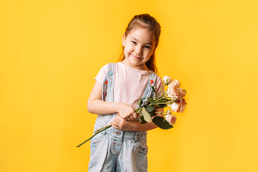 Girl holding spray roses in her hands against a yellow background.