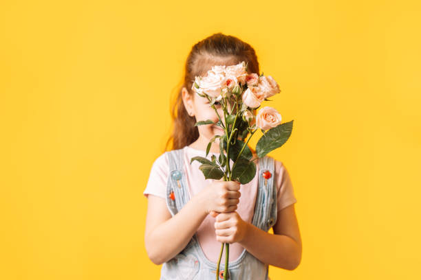 istock Child holding flowers in her hands against yellow background 2049277793