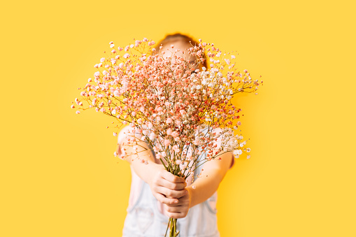 Little girl covering her face with flowers in front of a yellow background.