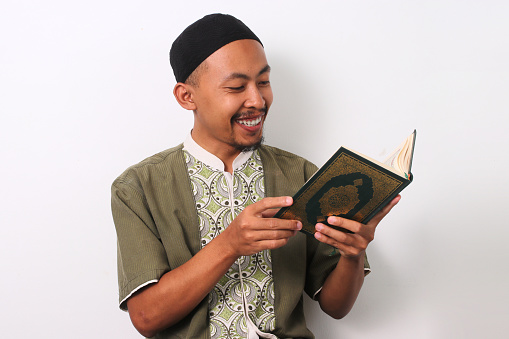 An Indonesian Muslim man reciting the Holy Quran with focus during Ramadan. Isolated on a white background