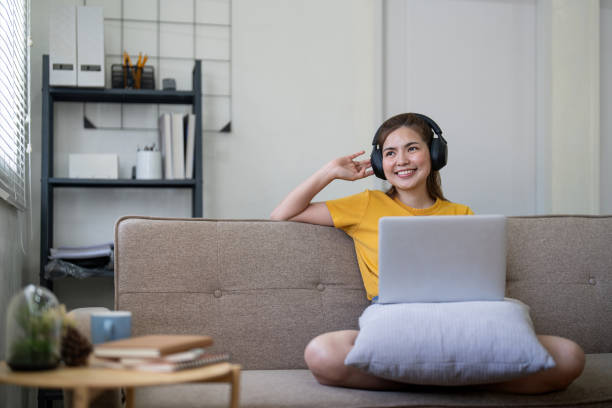 집에서 음악을 듣기 위해 노트북과 이어폰을 사용하는 젊은 아시아 여성 - room service audio 뉴스 사진 이미지