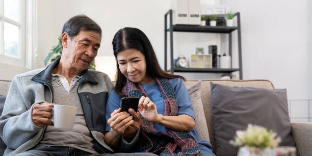 istock Happy elderly asian couple using smartphone sit on sofa doing ecommerce shopping online on website at home 2049391122
