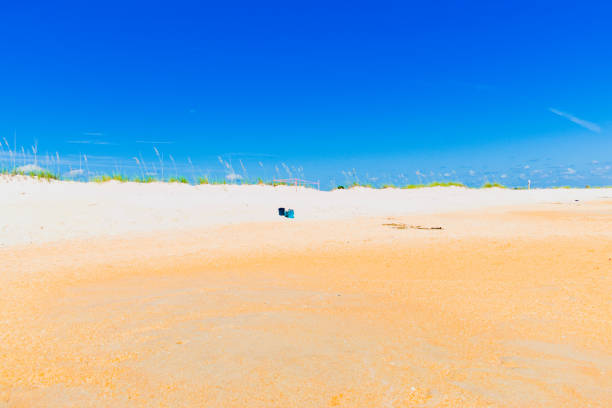 Flagler Beach, FL, USA, Sept 4, 2023: Some blue buckets on the brown sandy beach, blue sky as background.