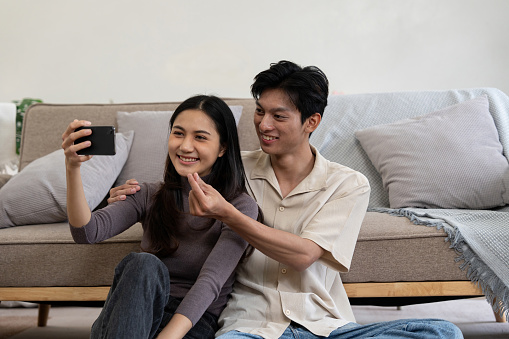 Happy couple asian young women happy smile and taking selfie on couch in living room at home.