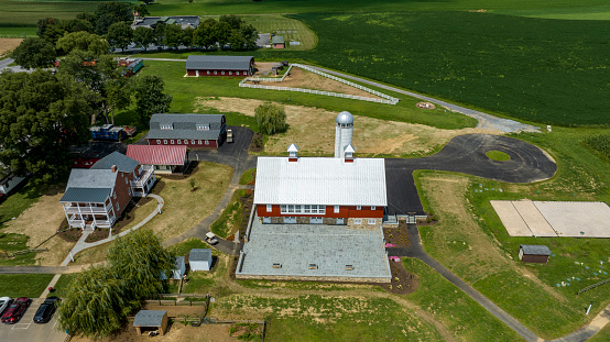 Aerial View Of A Rural Landscape Showing Multiple Red And White Buildings, A Silo, Green Fields, And Winding Paths.