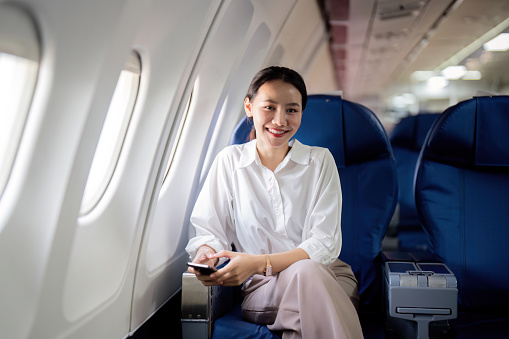 Successful asian businesswoman or female entrepreneur in a plane sits in a business class seat.