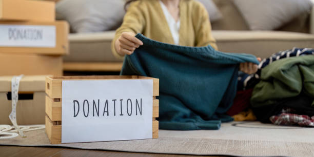 istock Donation, asian young woman sitting pack object at home, putting on stuff into donate box with second hand clothes, charity helping and needy people. Reuse recycle 2049480018