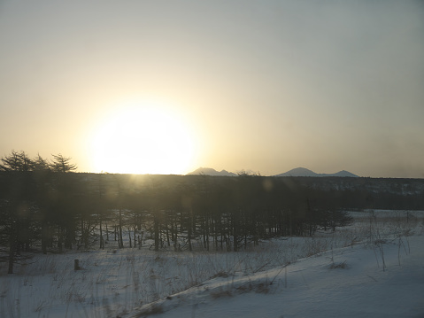 Driving in wilderness with sun rising over mountain ridge on winter Iturup, Kuril islands