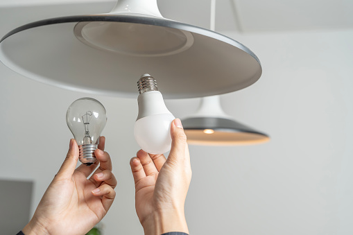 Energy saving idea: Asian people replace fluorescent light bulbs (CFL) with new LED bulbs. Female hands screw in an energy-saving LED light bulb.