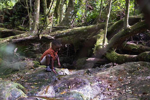 A young boy is playing in a river, he is on an adventure hike with his family.