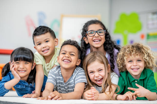 Kindergarten Portraits A small group of Kindergarten children lay tightly together on the floor of their classroom as they pose for a portrait. They are each dressed comfortably and are smiling. elementary student stock pictures, royalty-free photos & images