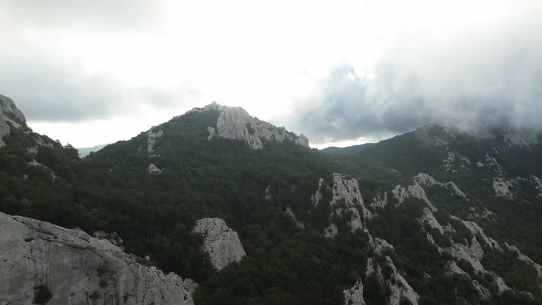 Drone flight towards the mountains in Croatia's Velebit National Park on a cloudy morning. Sun peeking behind the mountains.