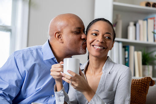 In their cozy home, a lovely mature woman shares a cup of coffee with her husband in the morning