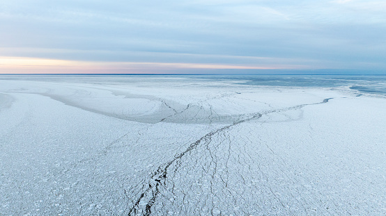 Aerial sunset colored panoramic view of the calm sea bay with the edge of the cracked sea ice and open water