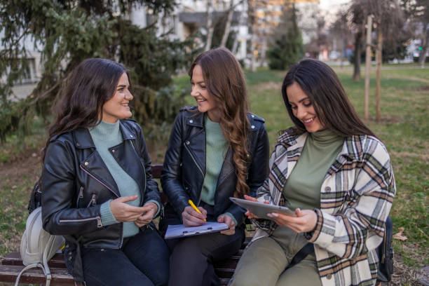 istock Female students sitting on the bench in public park, talking and laughing. 2049828775