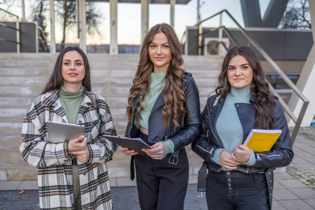 Three college student female friends smiling ready for classes in front of the university.