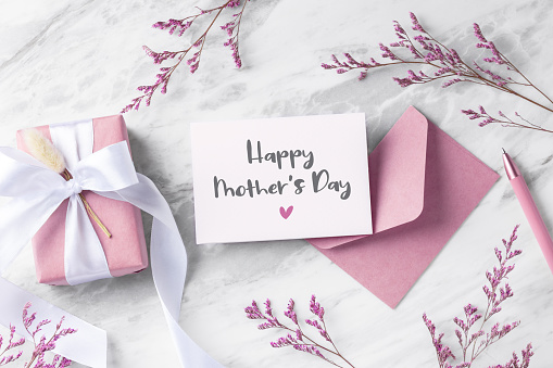 Happy mother's day card with pink gift box and envelope on marble table with flower, flatlay