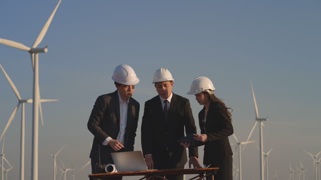 Engineers Examining Wind Farm Site with Blueprints and Laptop