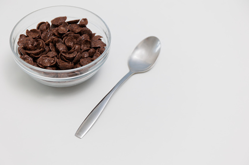 Chocolate cereals served in glass bowl with spoon on white background with copy space