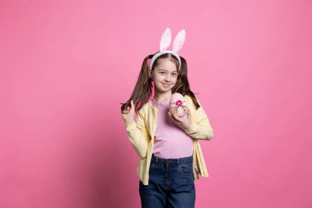 istock Little young girl with fluffy bunny ears shows a pink easter egg 2049915880