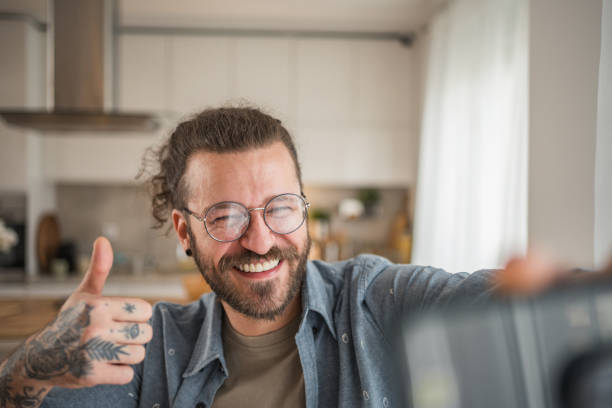 istock A man is standing in the kitchen, holding a cup of coffee, talking on a video call or taking selfies for social networks with a happy smile on his face 2049918575