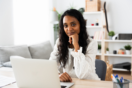 Portrait of Indian entrepreneur looking at camera. Young woman working on laptop with copy space.