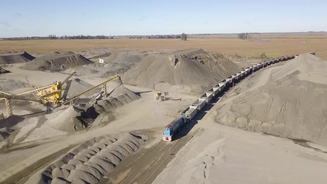 A busy quarry in argentina with heavy machinery, train being loaded and long conveyor belts, aerial view