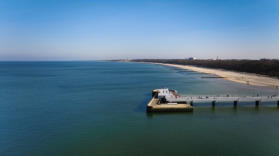 Koobrzeg pier on a sunny February afternoon. Windless weather, calm sea without a single wave, tourists strolling on the pier. Serene atmosphere captured in a stock photo.