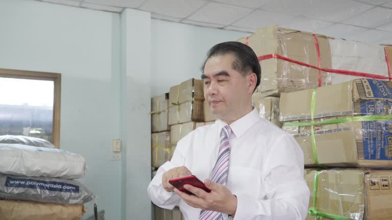 factory concept, Elderly Asian male businessman is using a business phone in a factory.