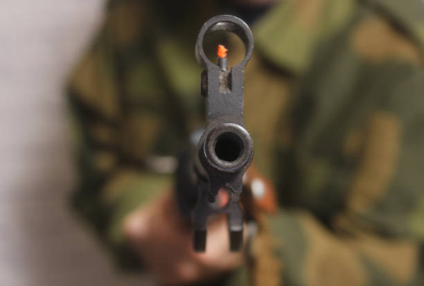 A person in a green jacket, holding a gun